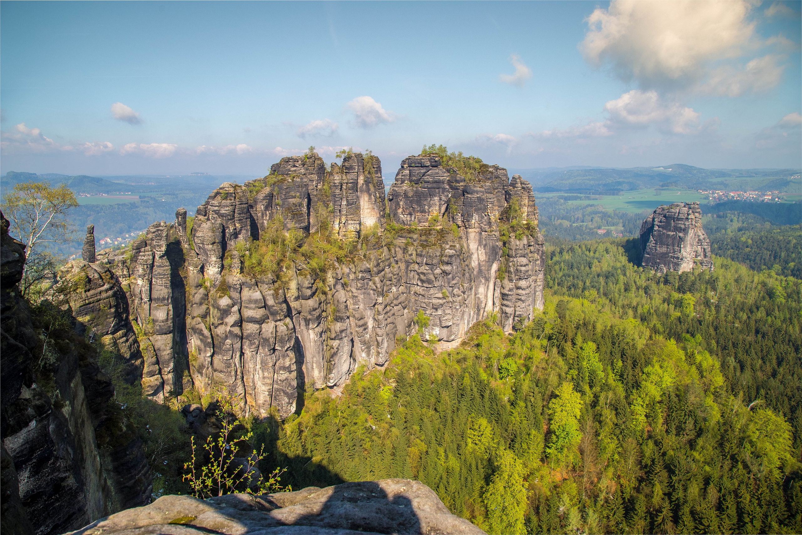 Blick auf die Schrammsteine im Nationalpark Sächsische Schweiz. Rundherum liegen Wälder und Wiesen. 