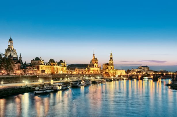 Auf der Elbe liegen Dampfschiffe. Dahinter erhebt sich die barocke Silhouette der Stadt Dresden. 